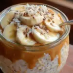 Peanut butter banana overnight oats in a glass bowl topped with sliced bananas and nuts.