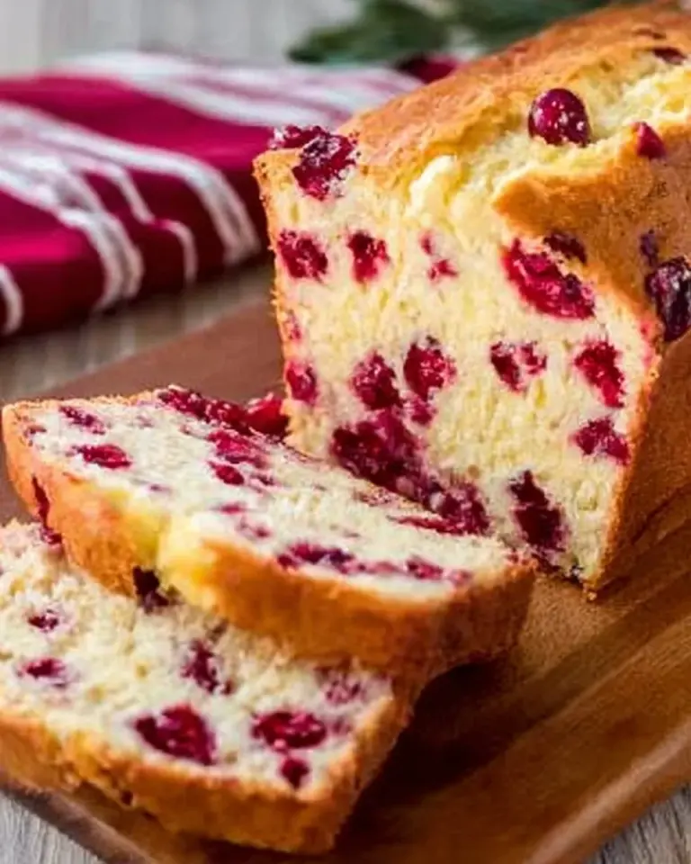 Sliced Cream Cheese Cranberry Bread on a wooden board with cranberries.