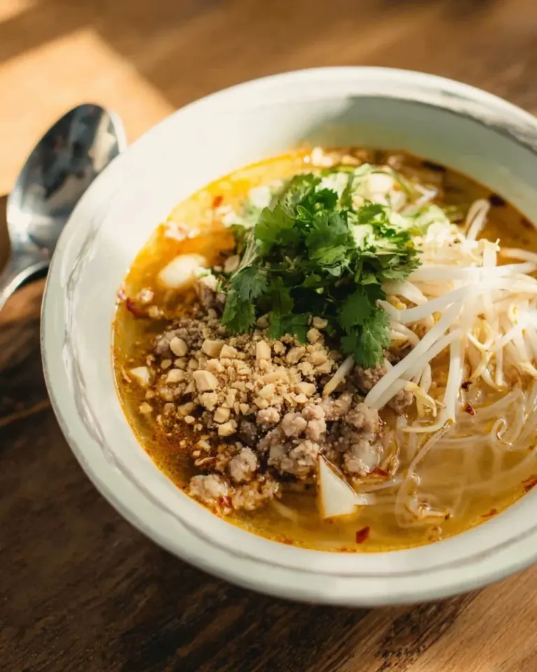 Bowl of Thai spicy and sour noodle soup garnished with fresh herbs and chili.